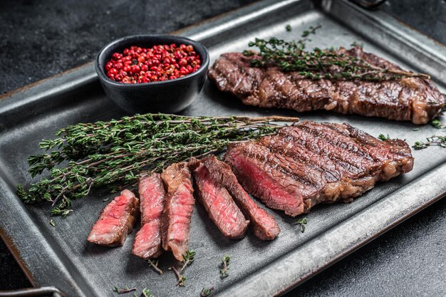 BBQ Roast Denver Top Blade Beef Steak auf einem Stahlblech mit Kräutern Schwarzer Hintergrund Draufsicht