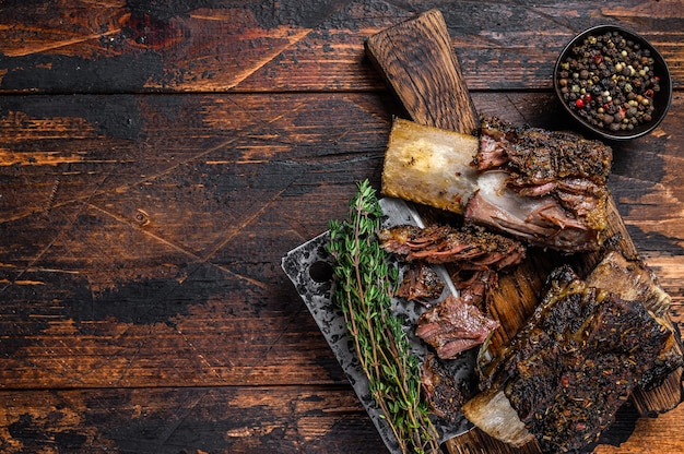 BBQ Short Chuck Beef Ribs mit Kräutern und Fleischerbeil. Dunkler hölzerner Hintergrund. Ansicht von oben. Platz kopieren.