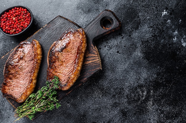 BBQ Tapa de solomillo a la parrilla o bistec picanha sobre una tabla de cortar de madera. Fondo negro. Vista superior. Copie el espacio.