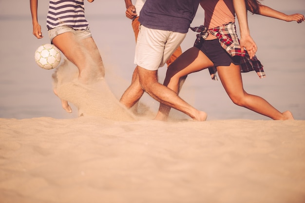 Beachball in Bewegung. Abgeschnittenes Bild von jungen Leuten, die mit Fußball am Strand spielen