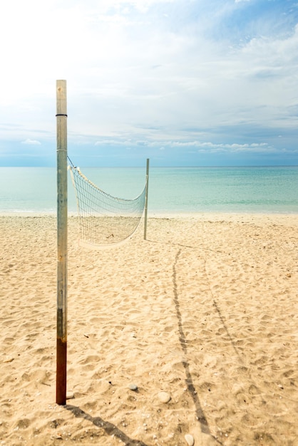 Beachvolleyballnetz an einem goldenen Sandstrand mit türkisfarbenem Meerwasser und hellblauem, sonnigem Himmel