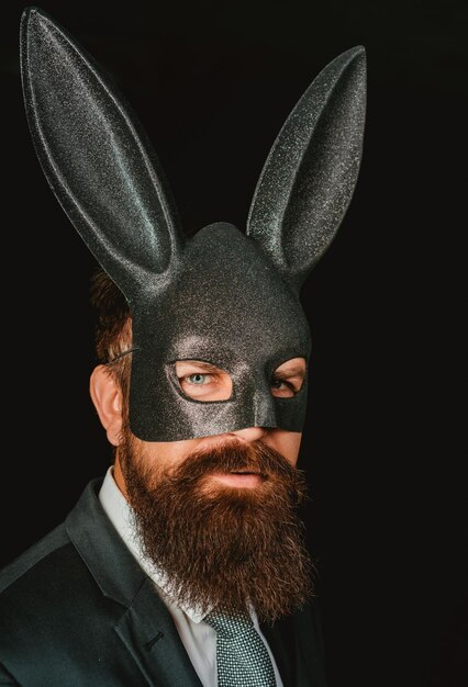 Bearded Hipster in Anzug ist bereit für den Karneval lustiger Bearded Man in Karneval Kaninchenmaske hübscher Mann in Karnevalsmaske Ballsaal Kaninchen mit langen Ohren sinnlich auf schwarzem Hintergrund