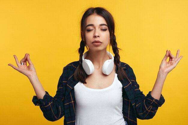 Beauiful joven mujer hace que el signo de mudra se relaja después de un duro día de trabajo mantiene los ojos cerrados practica yoga. Mujer bonita joven medita interior. Concepto de relajación