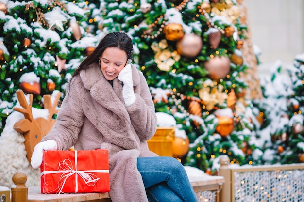 Beautidul chica con regalo rojo en Navidad con smartphone en la nieve al aire libre