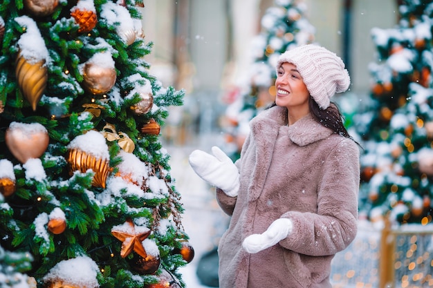 Beautidul mujer cerca del árbol de Navidad en la nieve al aire libre