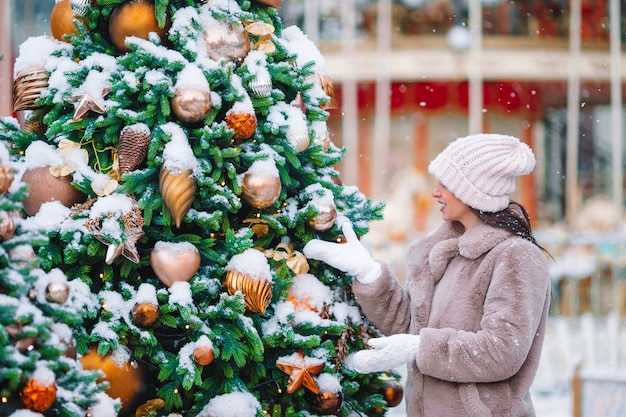 Beautidul mujer cerca del árbol de Navidad en la nieve al aire libre