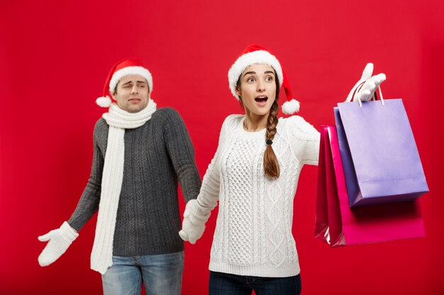 Beautiful girlfriend forçar seu namorado a fazer compras no fundo vermelho de Natal.