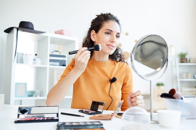 Beauty-Bloggerin, die Konturpuder auf ihrem Gesicht unter Verwendung des Make-up-Pinsels, horizontaler Low Angle Shot aufträgt