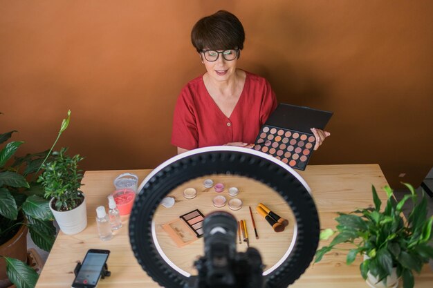 Beauty-Bloggerin oder Influencerin mittleren Alters mit Make-up-Produktaufnahmevideo im Zimmer zu Hause
