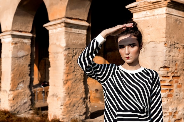 Beauty Fashion Model Girl mit braunen Haaren auf dem Hintergrund eines alten, verlassenen Gebäudes, das stilvolle Kleidung trägt.