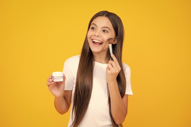 Beauty-Make-up und Kinderkosmetik Teenager-Kind-Mädchen mit Pinsel Anwendung erröten Gesicht isoliert auf wellow Hintergrund Happy Teenager-Porträt Lächelndes Mädchen