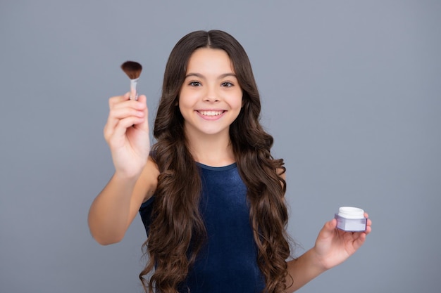 Beauty-Make-up und Kinderkosmetik Teenager-Mädchen 12 13 14 Jahre alt mit Pinsel Auftragen von Rouge auf Gesicht isoliert auf grauem Hintergrund Glückliches Mädchen Gesicht positive und lächelnde Emotionen