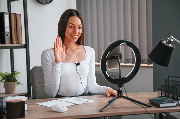 Foto beauty-meisterkurs per smartphone junge schöne frau in weißer kleidung ist im büro