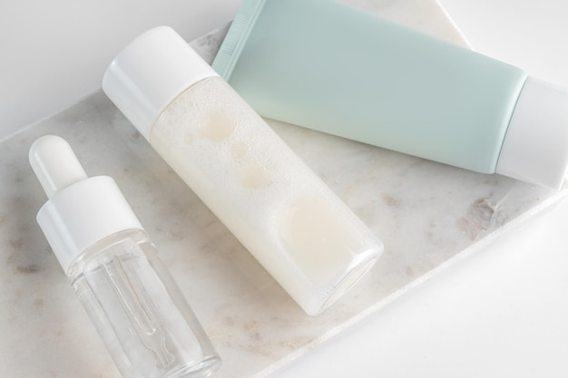 Beauty-Produktkonzept Tube mit Creme und Flaschen mit Serum und Lotion auf weißem Hintergrund auf Marmortablett Draufsicht Trendige Vitrine mit natürlichen Farben