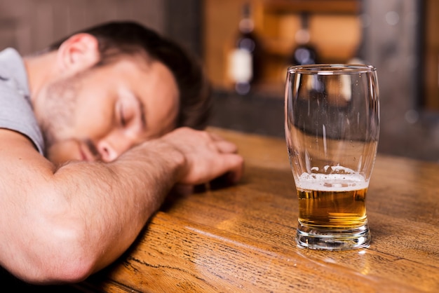 Bêbado de novo. Cliente do sexo masculino bêbado encostado no balcão do bar e dormindo enquanto um copo de cerveja está parado perto dele