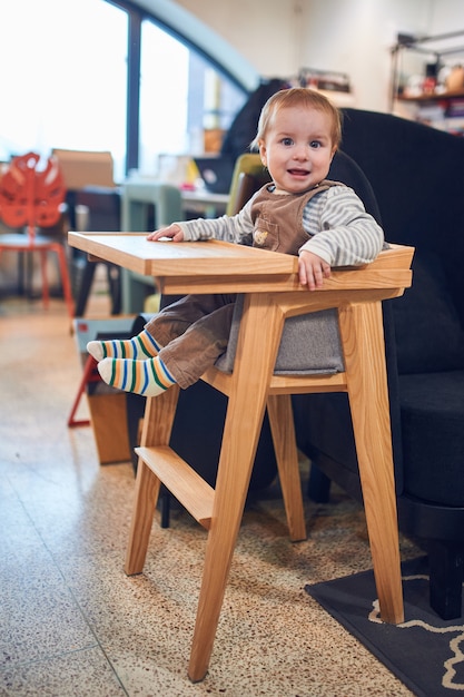 Foto bebé de 1 año sentado en una silla alta de madera en casa