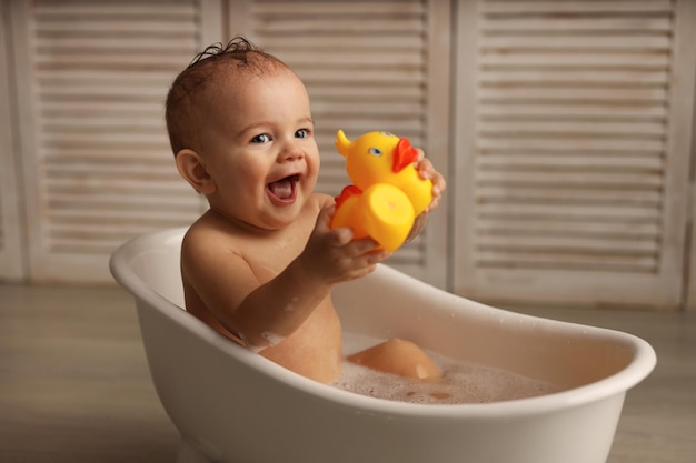 un bebé de 11 meses se está bañando en una bañera blanca con patitos de goma