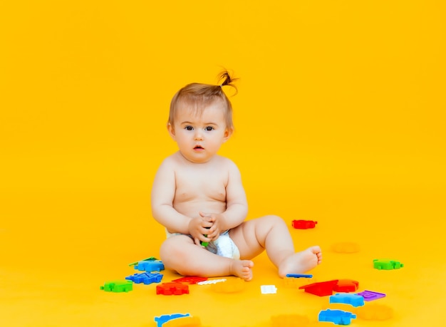 Bebé de 11 meses juega con juguetes sobre un fondo amarillo. retrato de un niño aislado sobre un fondo amarillo