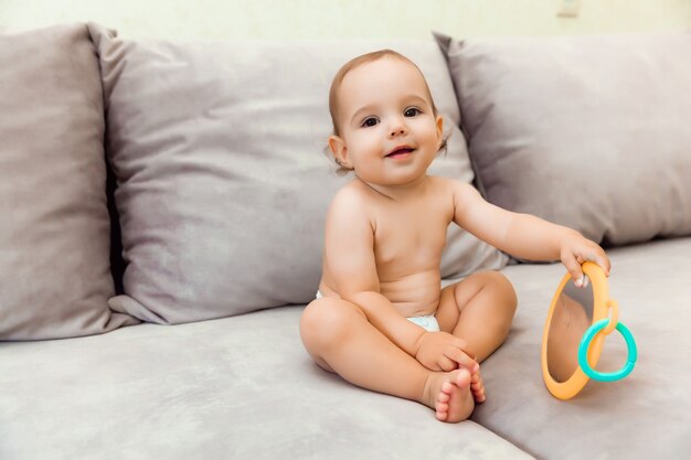 Bebé de 11 meses sentado en el sofá. lindo bebé en un pañal en el sofá sonriendo.