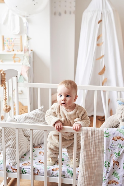 Bebé de 6 meses de pie en la cuna en la habitación de los niños. Feliz maternidad y paternidad. Clínica y hospital de maternidad. Día del padre y la madre. Desarrollo de la primera infancia, guardería.