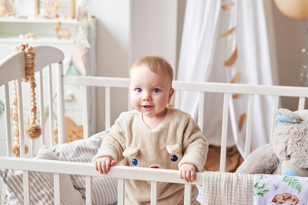 Bebé de 6 meses de pie en la cuna en la habitación de los niños. Feliz maternidad y paternidad. Clínica y hospital de maternidad. Día del padre y la madre. Desarrollo de la primera infancia, guardería.