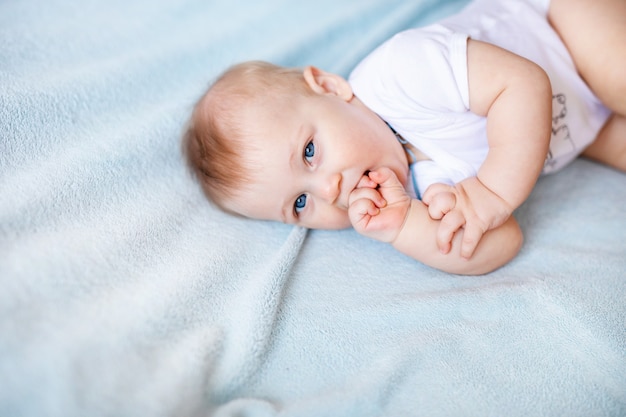 Bebé adorable en el dormitorio soleado blanco. Niño recién nacido relajante en una cama azul. Guardería para niños pequeños.