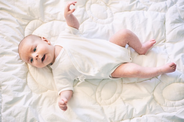 Bebé adorable en el dormitorio soleado blanco. Recién nacido infantil relajante en la cama.