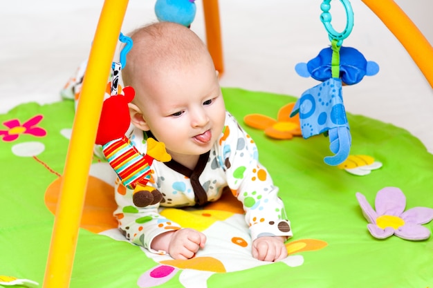 Bebé adorable que se divierte con los juguetes en la estera colorida del juego.