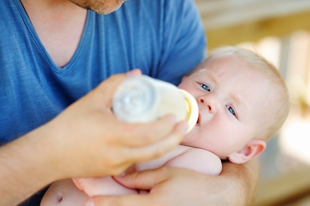 Bebé adorável que bebe o leite do frasco nas mãos do pai