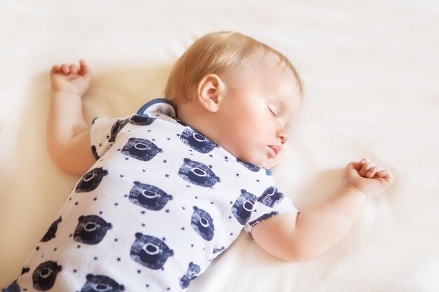 Bebê adorável tranquilo dormindo em sua cama com lençol branco em um quarto. Foco suave. Conceito de bebê dormindo. O bebé de 1 ano de pijama dorme em casa