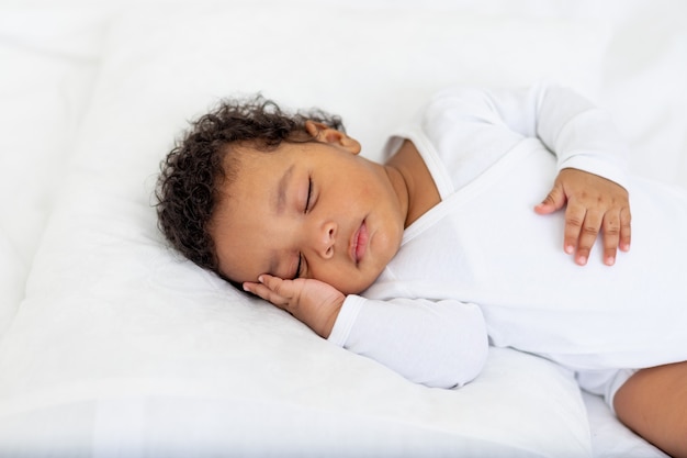 Bebé afroamericano duerme en una cama blanca en casa con la mano doblada debajo de la mejilla