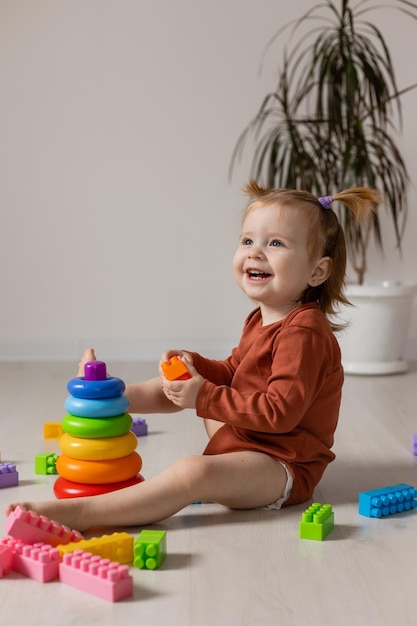 bebé alegre juega con una pirámide multicolor y otros juguetes educativos sentados en el suelo