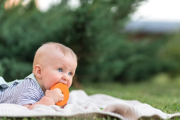 Bebé de hasta un año roe un juguete de madera en el verano en la naturaleza primer concepto de dentición