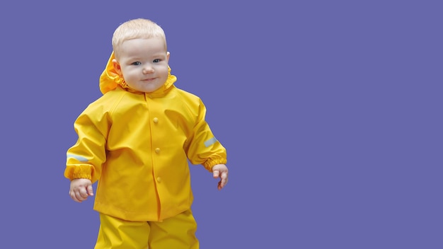 Bebé de un año con traje impermeable amarillo sobre fondo morado