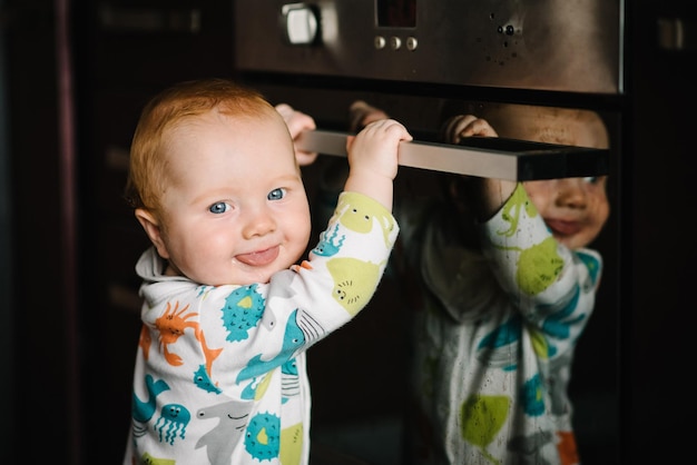 El bebé aprende a pararse cerca del horno en la cocina El pequeño bebé de nueve meses se para con apoyo en casa El niño pequeño acaba de aprender a pararse sobre sus pies Cerrar