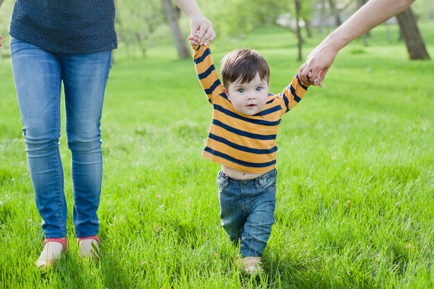 Bebê aprendendo a andar com a ajuda das mãos de mães e pais