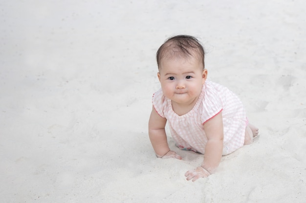 Bebé asiático gateando sobre la arena