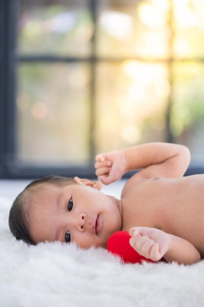 Foto un bebé asiático muy joven está acostado en una cama blanca y el bebé mira a su alrededor