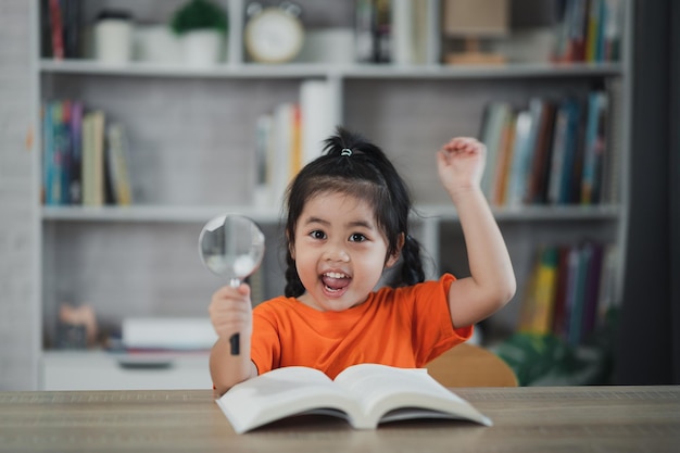 Bebé asiático niño niña sosteniendo lupa y levanta la mano leyendo libro educación niños y escuela concepto feliz sonriente estudiante niña aprendiendo a estudiar Educación desarrollo concepto