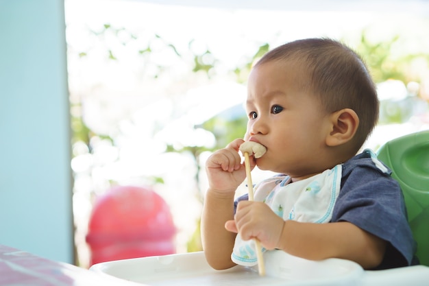 Bebé asiático que come la comida solo