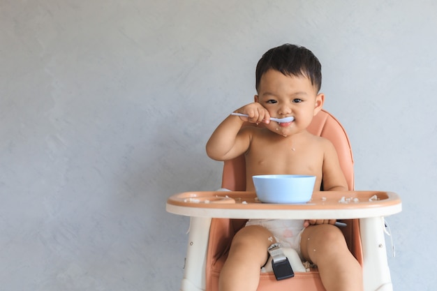 Bebé asiático que come la comida solo