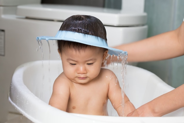 Bebé asiático tomando un baño de mamá y vistiendo gorro de ducha