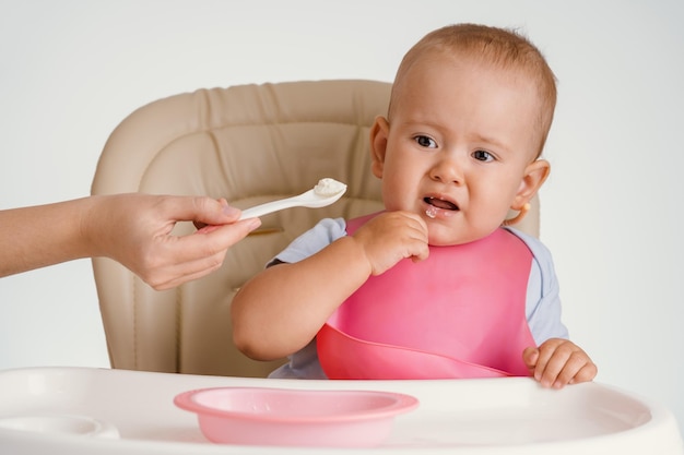 Un bebé con un babero rosa se niega a comer con cuchara