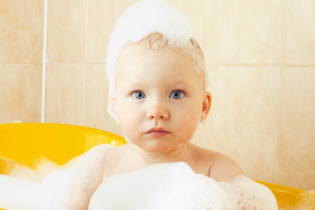 El bebé se baña en un baño amarillo con burbujas y espuma. El concepto de niño feliz, amor por bañarse.