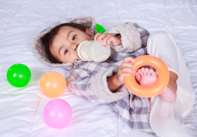 Foto bebê bebendo leite com garrafa na cama