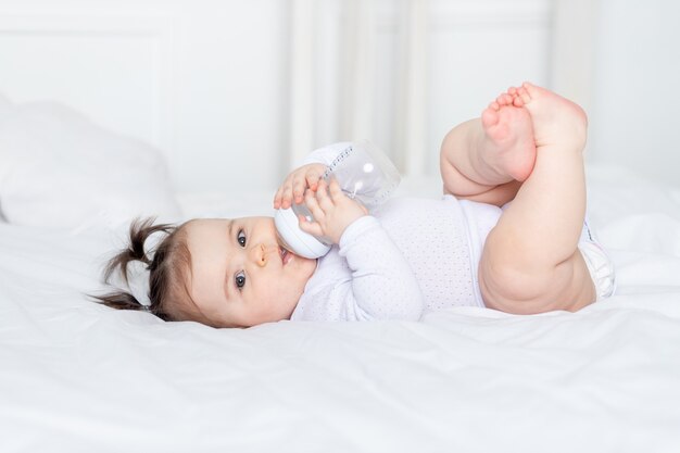 Bebé con un biberón en la cama en casa, concepto de comida para bebés