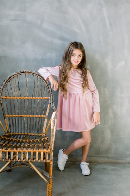 Bebê bonito 5-6 anos de idade usando vestido elegante rosa overgrey fundo. Olhando para a câmera. Festa de aniversário. Celebração.