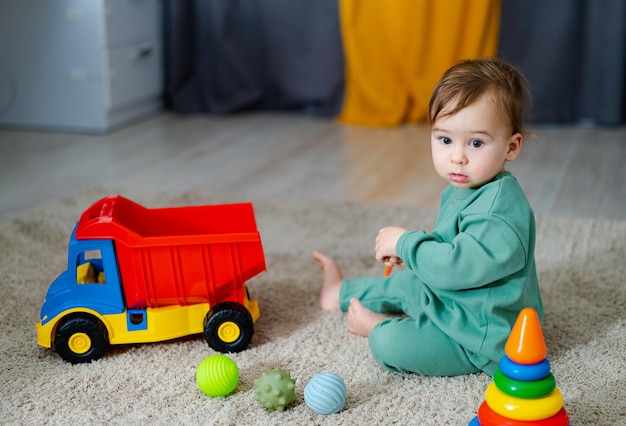 Bebê bonito e alegre brincando com brinquedos coloridos em casa Criança com caminhão de brinquedo Criança com brinquedo educacional Desenvolvimento inicial