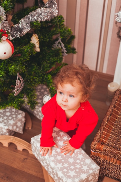 Bebé bonito feliz vestido con vestido rojo con regalos de Navidad