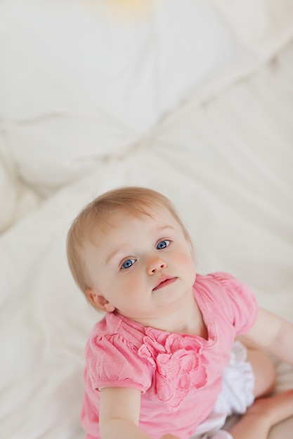 Bebê bonito olhando a câmera enquanto está sentado em uma cama